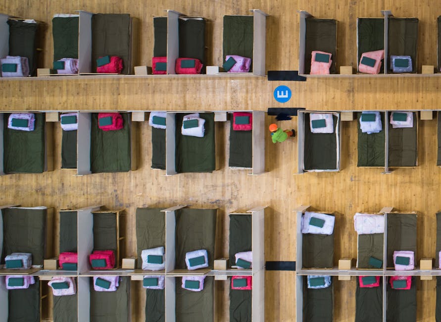 Top-down view of an emergency shelter with arranged beds in rows and worker present.